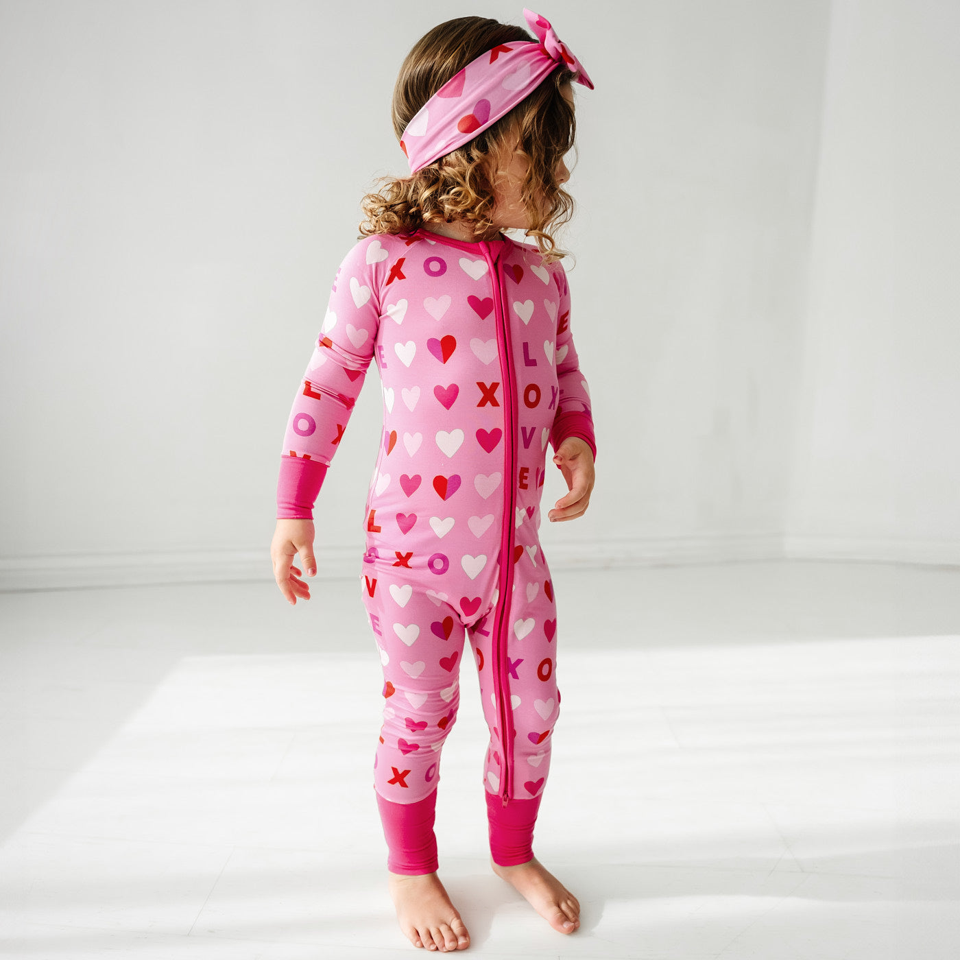 Child wearing a Pink XOXO zippy paired with a matching luxe bow headband