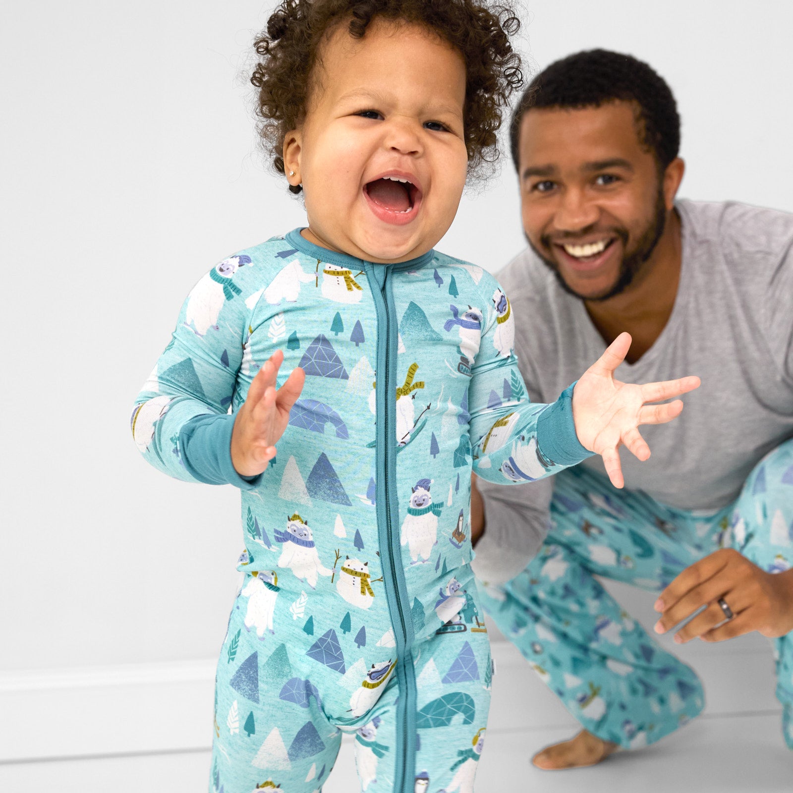 Child playing wearing a Yeti Snow Day zippy. Dad is matching wearing a men's Heather Gray pj top and men's Yeti Snow Day pants