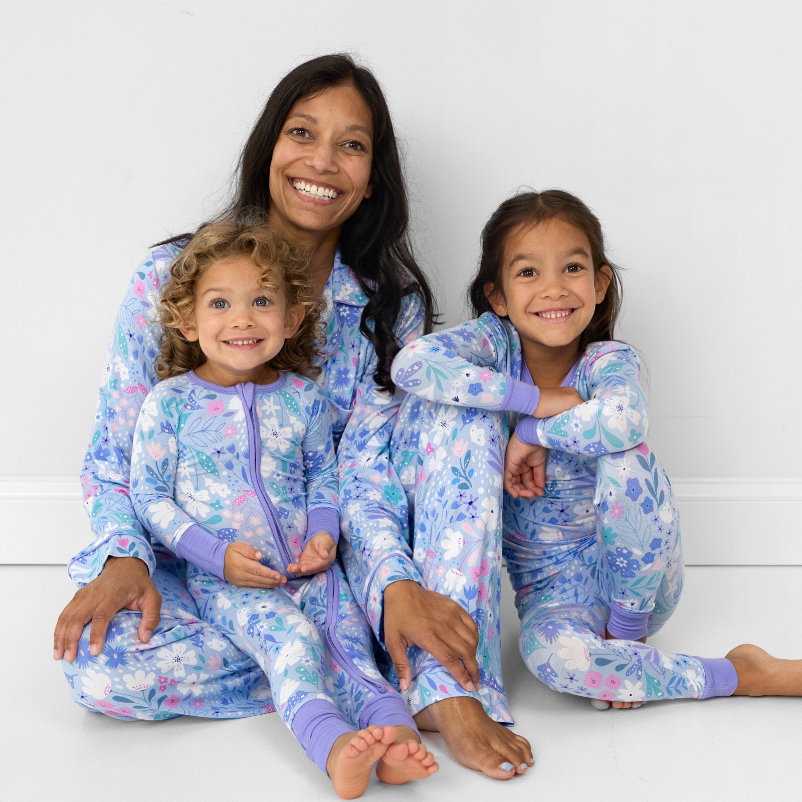 image of a mom and her two children wearing matching Magical Meadow pj sets. Mom is wearing women's two piece pj set and children are wearing two piece and zippy styles