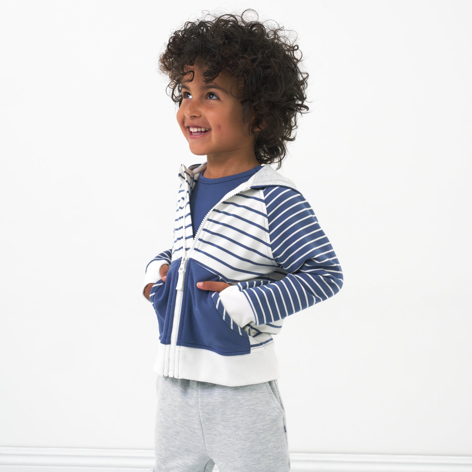 Child posing with their hands in their pockets wearing a Vintage Navy and Ivory Stripes zip hoodie paired with light heather gray shorts