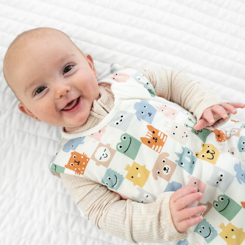 Close up image of a child laying on a blanket wearing a Check Mates sleepy bag and Heather Oatmeal zippy. 