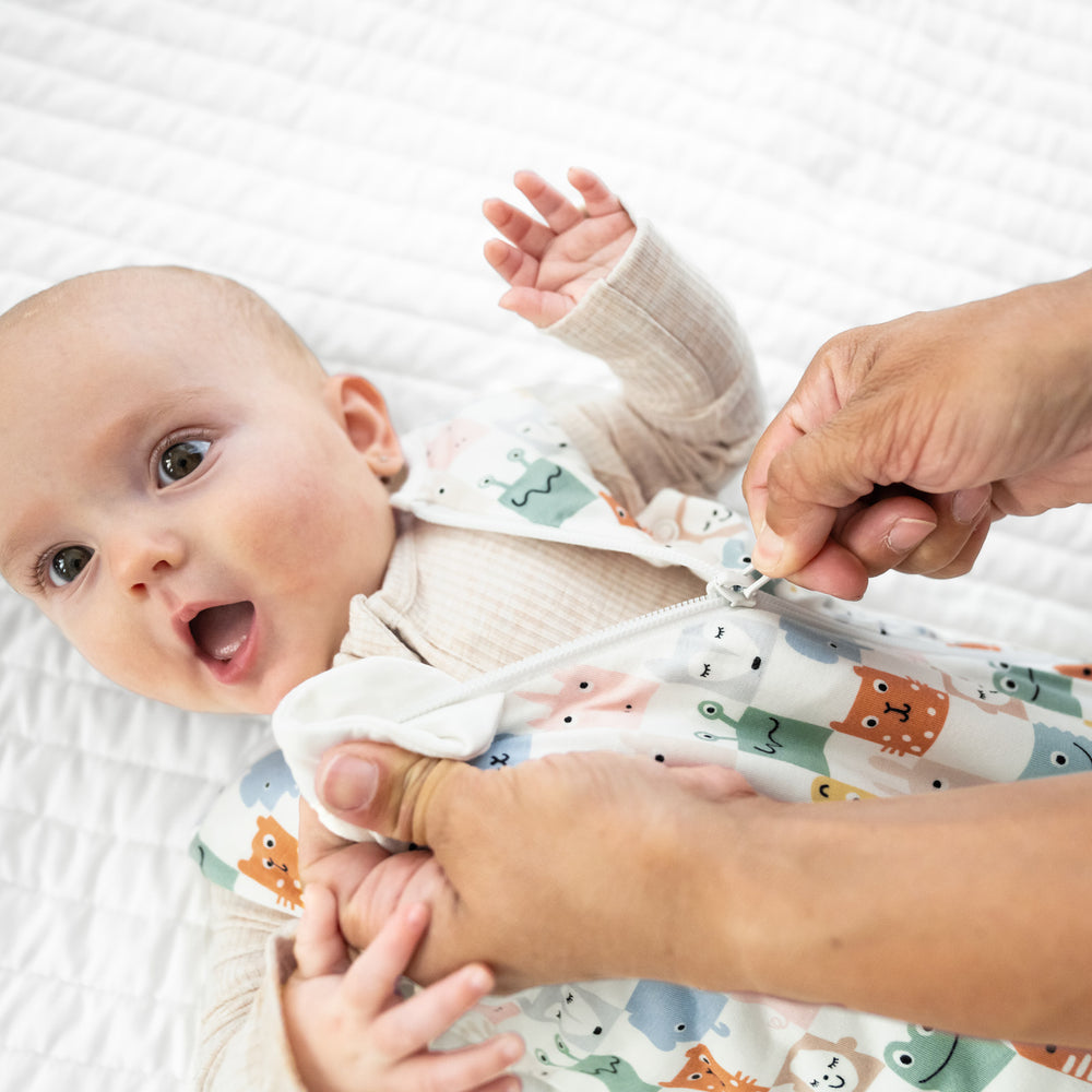 Close up image of a child laying on a blanket wearing a Check Mates sleepy bag and Heather Oatmeal zippy. Mom is demonstrating the zipper