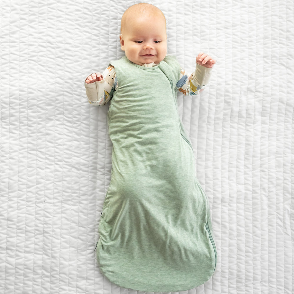 Child laying on a bed wearing a Heather Sage Sleepy bag over a Check Mates zippy