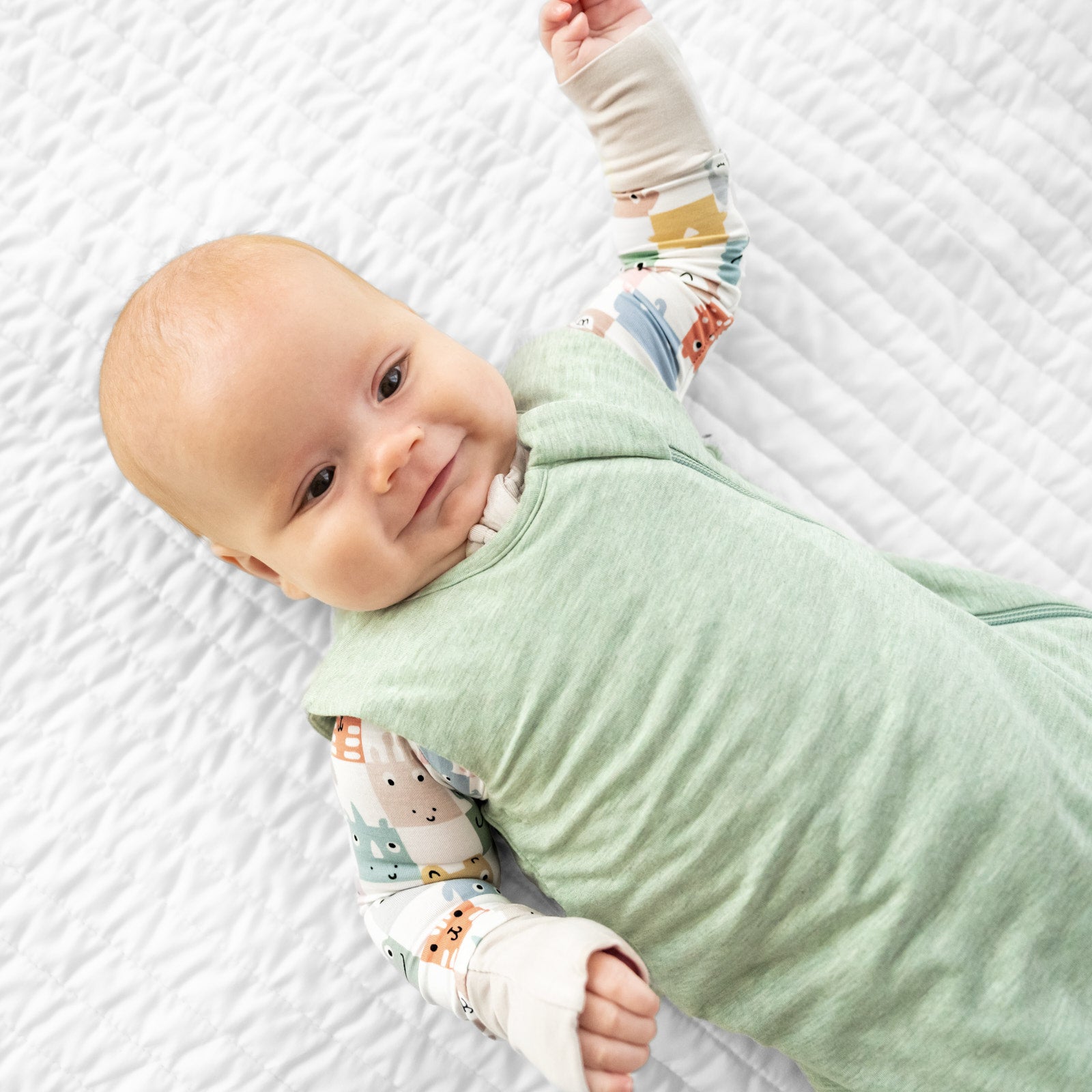 Close up image of a child laying on a bed wearing a Heather Sage Sleepy bag over a Check Mates zippy