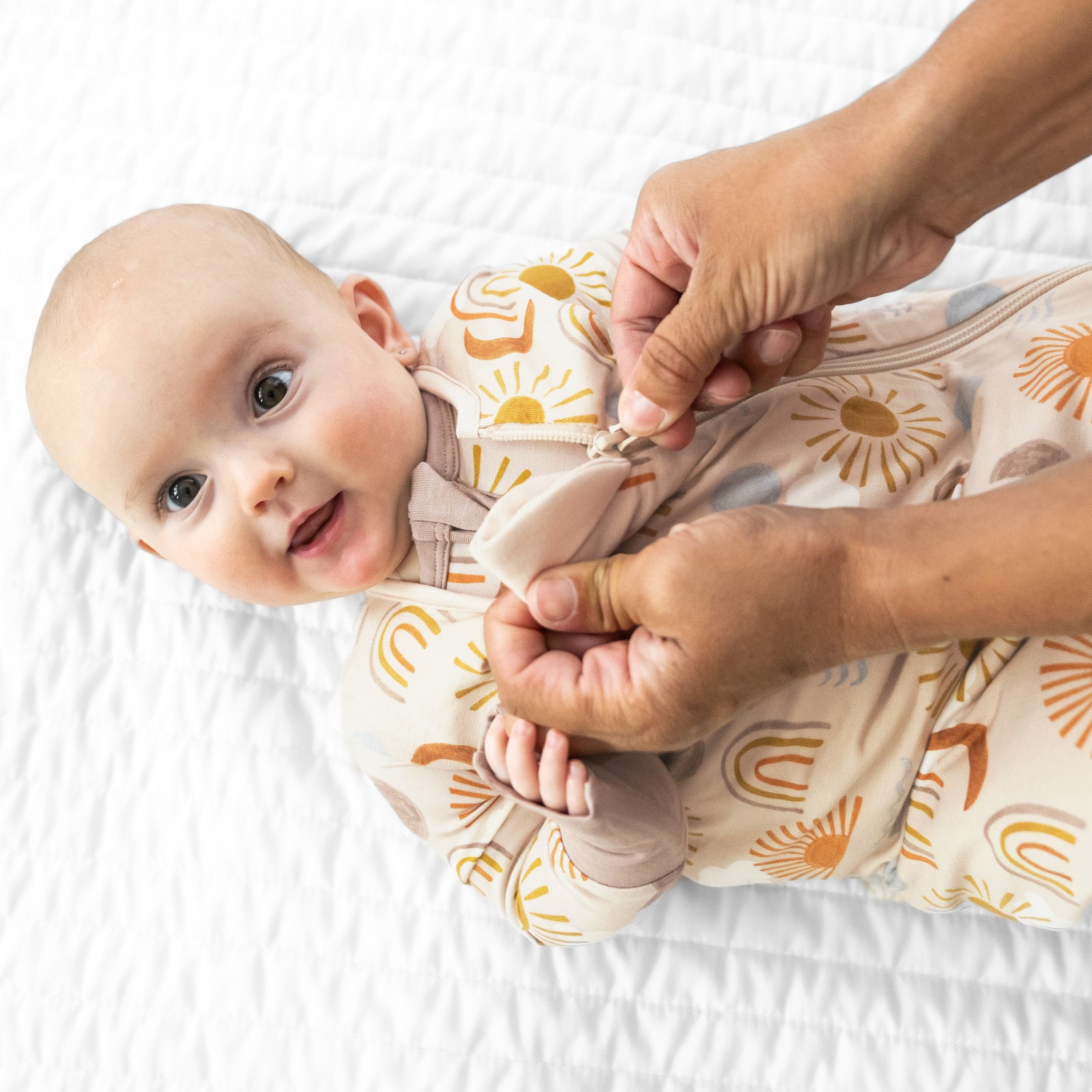 Close up image of a child laying on a blanket wearing a Desert Sunrise sleepy bag and matching zippy. Mom is demonstrating the zipper