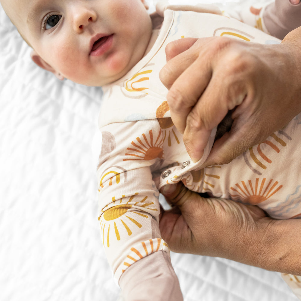 Alternate close up image of a child laying on a blanket wearing a Desert Sunrise sleepy bag and matching zippy. Mom is demonstrating the underarm snaps