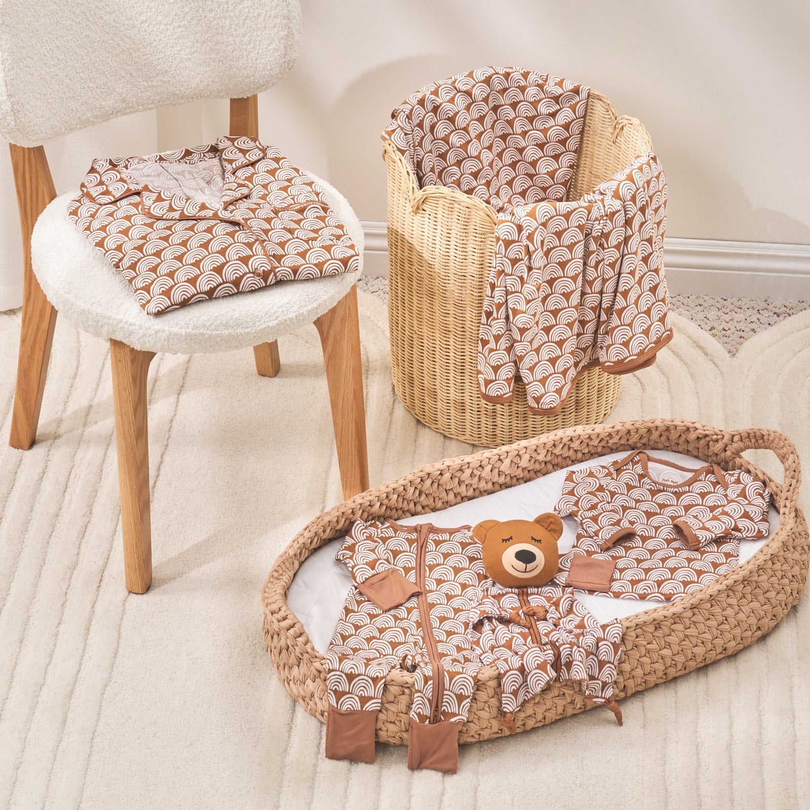 still life photo of rust rainbows zippy, lovey, gown, womens sleep shirt and blanket on top of a chair, basket and basinette