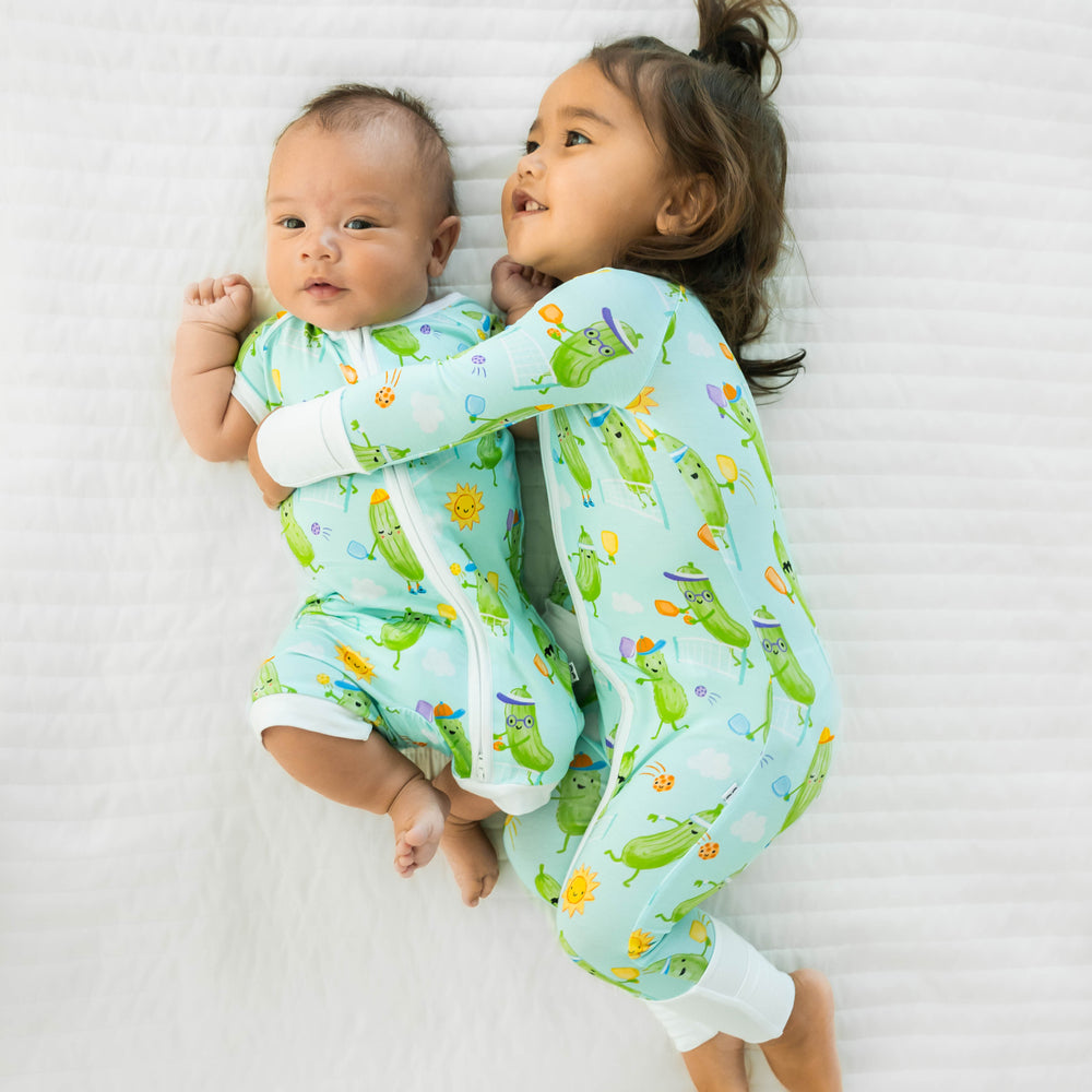 Two children wearing the Pickle Power print. Baby on the left is wearing the Pickle Power Shorty Zippy and child on the left is wearing the Pickle Power Zippy