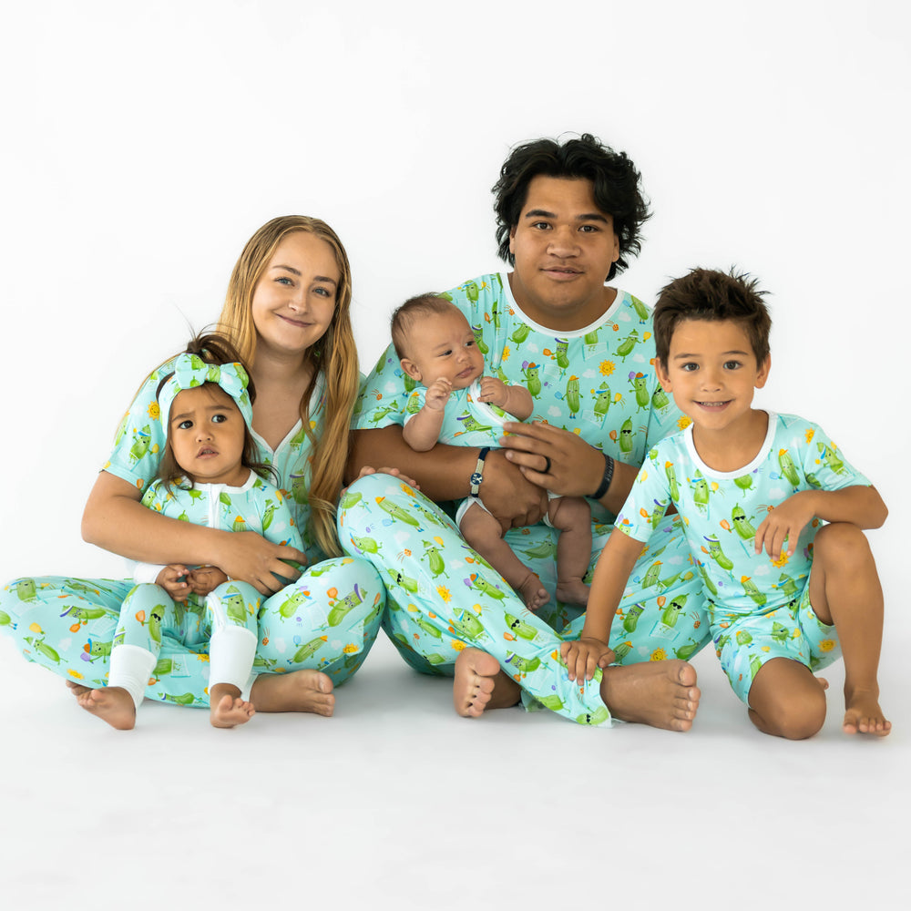 Family sitting while wearing the Pickle Power print. Mother is to the left wearing the Pickle Power Women's Short Sleeve Top and Pants. The daughter is wearing the Pickle Power Zippy and Pickle Power Luxe Bow Headband. Father in the middle is wearing the Pickle Pear Men's Short Sleeve Top and Pants, while holding baby wearing the Shorty Zippy. Boy on the right is wearing the Pickle Power Short-sleeve Pajama Set.