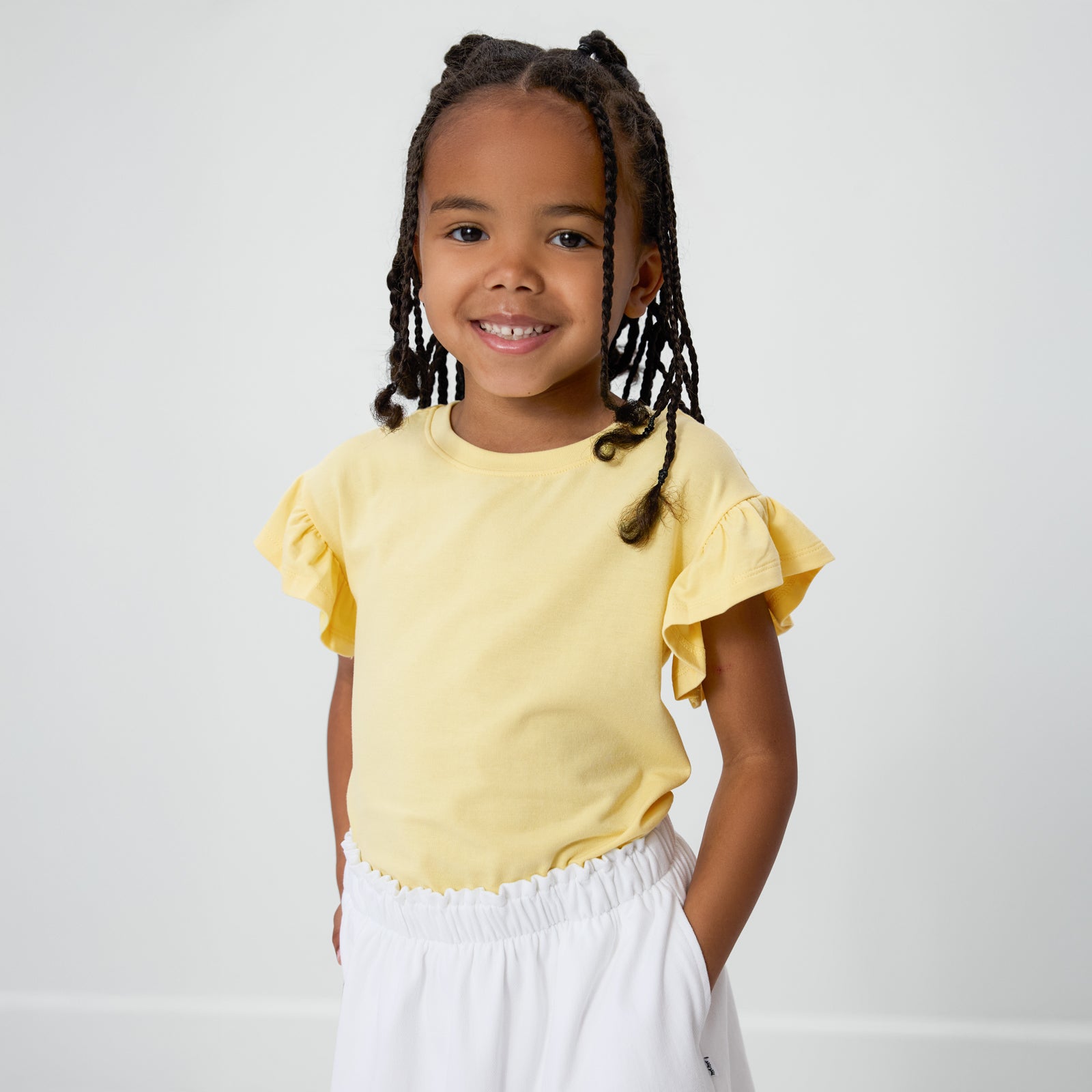 Child wearing the Lemon Twist Ruffle Tee with bright white denim shorts