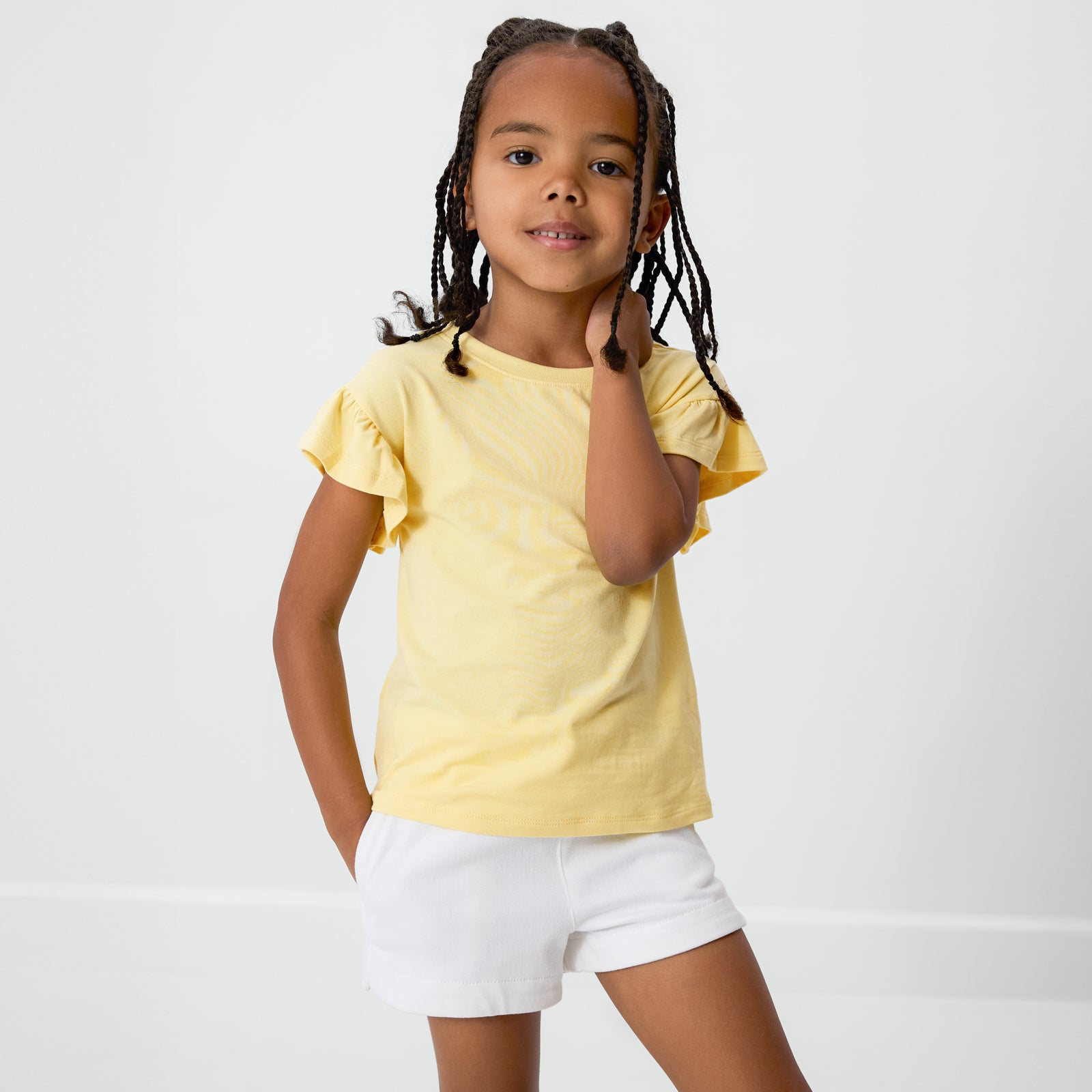 Posing child wearing the Lemon Twist Ruffle Tee with bright white denim shorts