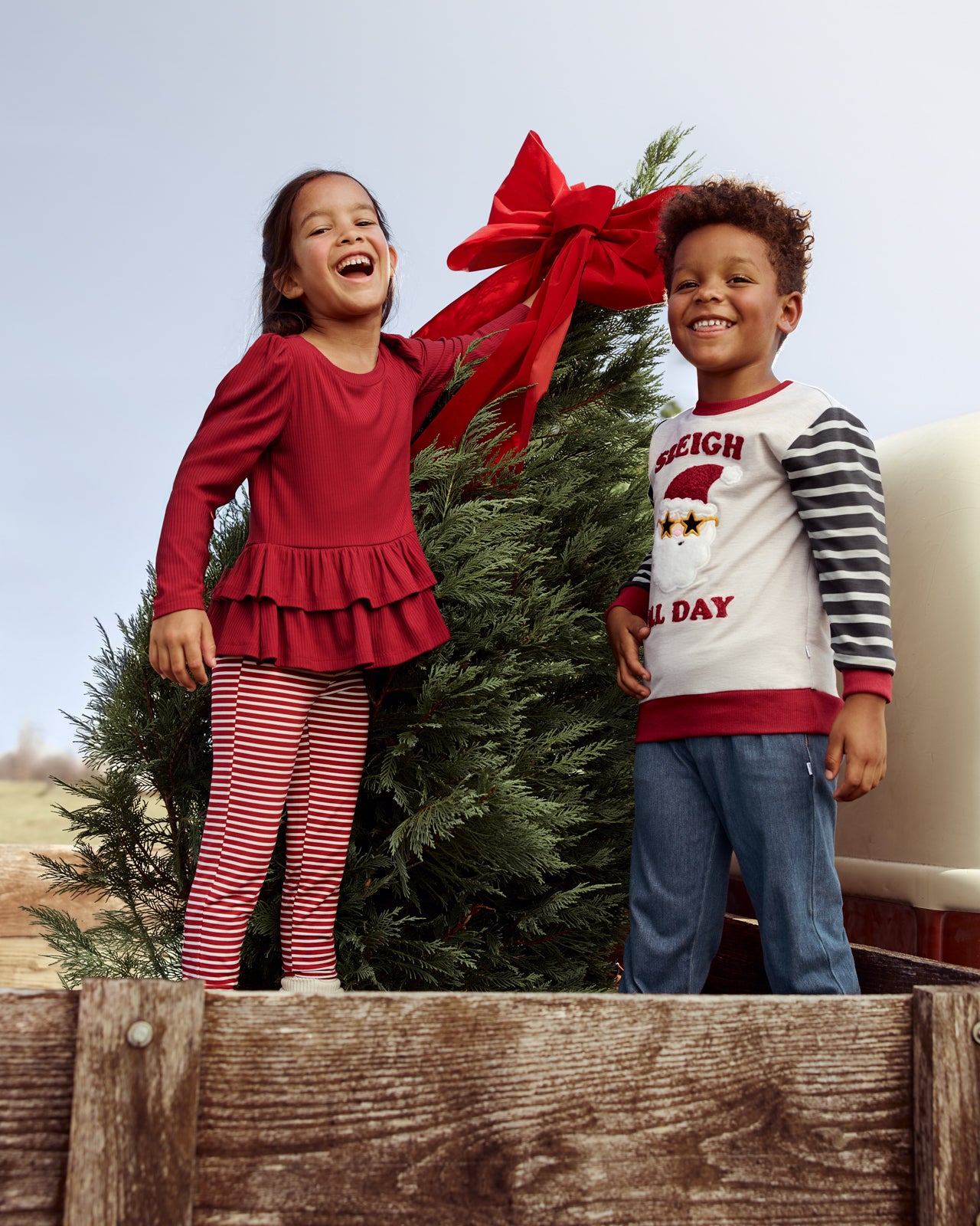 Two children at a Christmas tree farm wearing Holiday Play styles