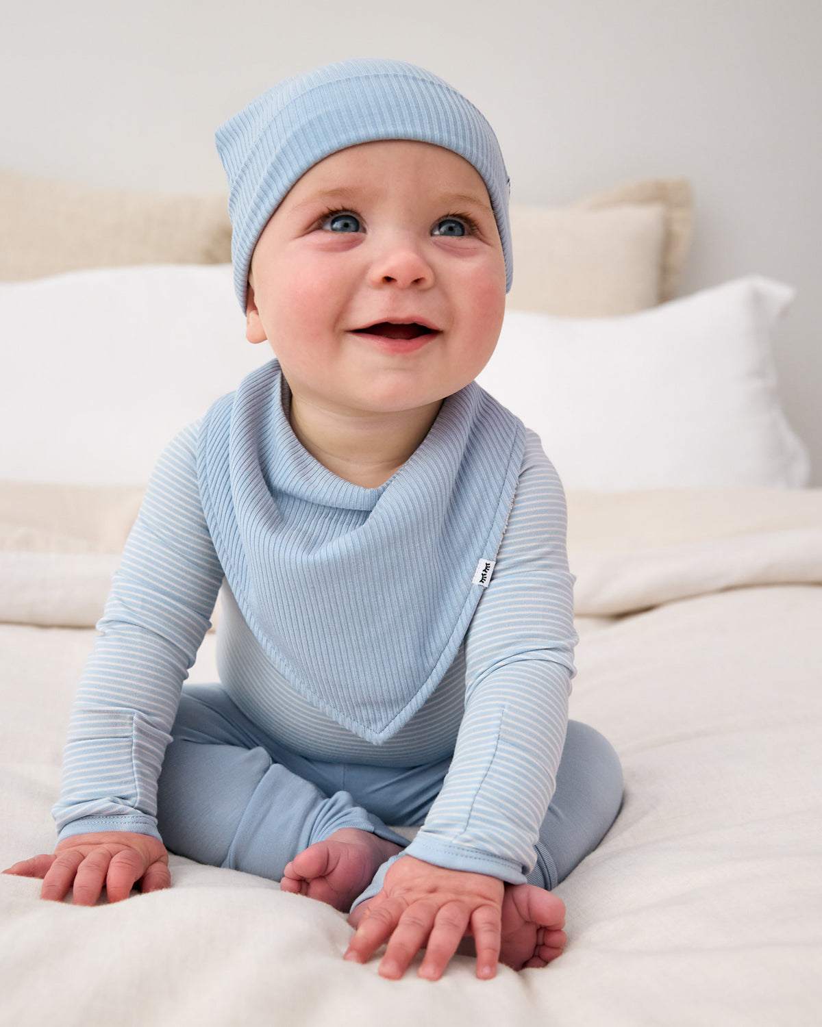 Sitting newborn wearing the Light Fog Ribbed Bandana Bib with a matching hat