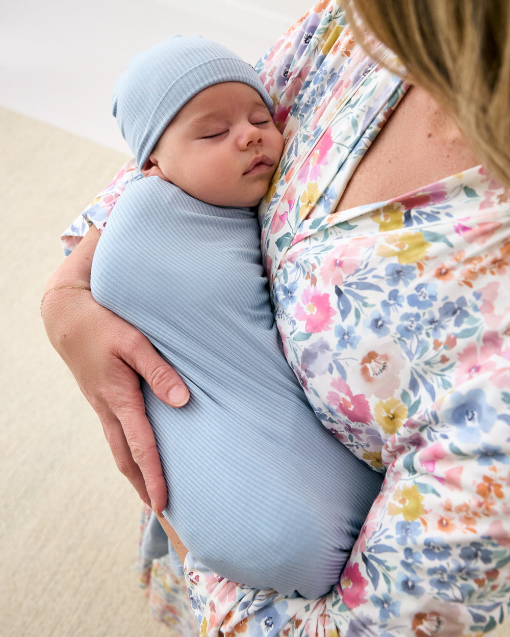 Mother holding baby swaddled in the Light Fog Baby Ribbed Swaddle & Infant Beanie Set