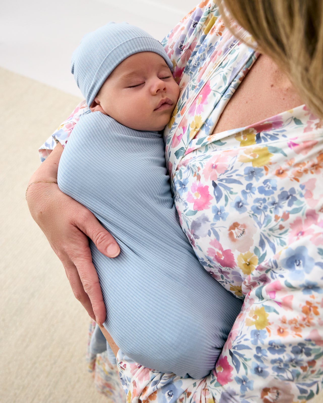 Mother holding baby swaddled in the Light Fog Baby Ribbed Swaddle & Infant Beanie Set