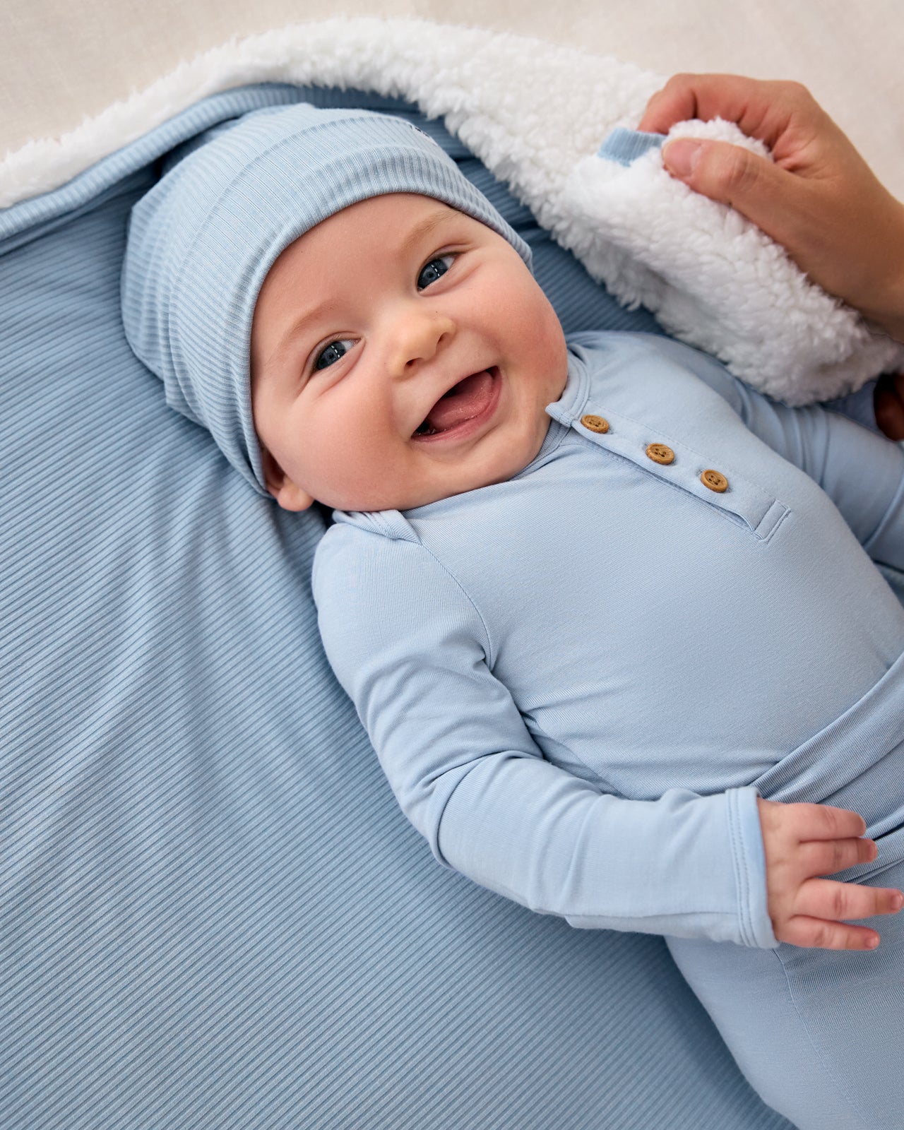 Baby wearing the Light Fog Ribbed Infant Beanie laying on a blue baby blanket