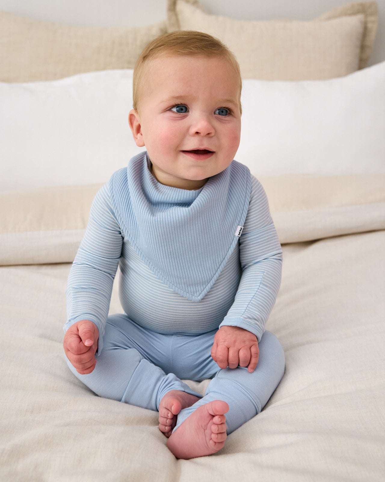 Sitting baby wearing the Light Fog Ribbed Bandana Bib with a matching newborn boy outfit