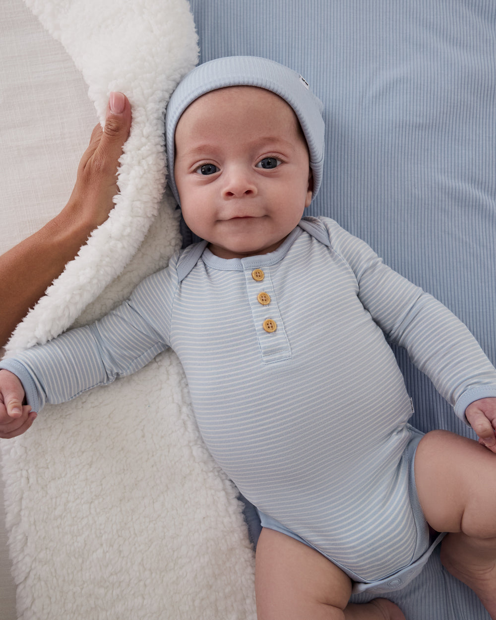 Baby wearing the Light Fog Stripe Henley Bodysuit on a blue baby blanket