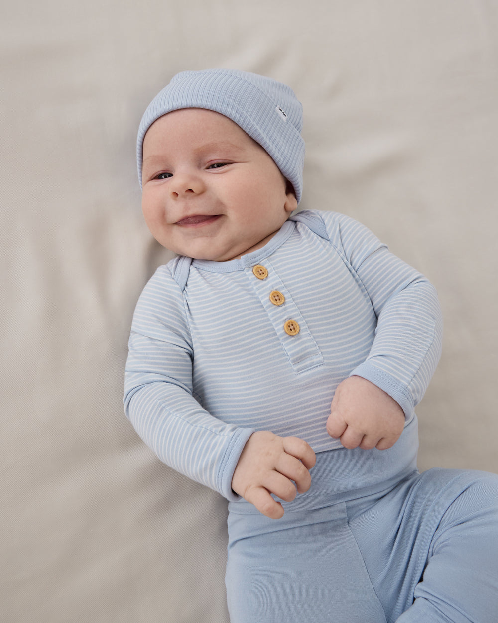 Baby wearing the Light Fog Stripe Henley Bodysuit with blue baby leggings