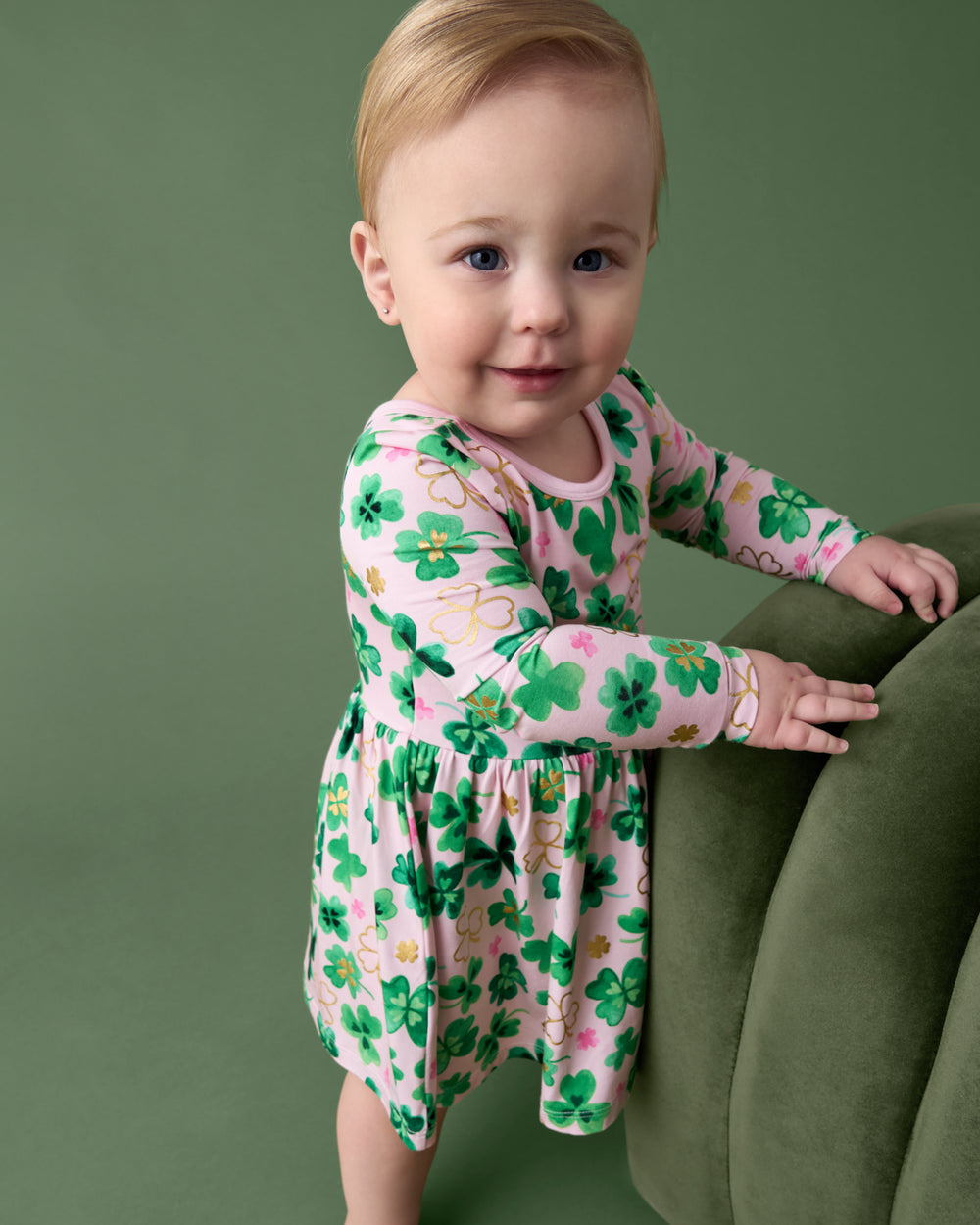 Baby wearing the Clover Cuties Twirl Dress with Bodysuit on a green back drop