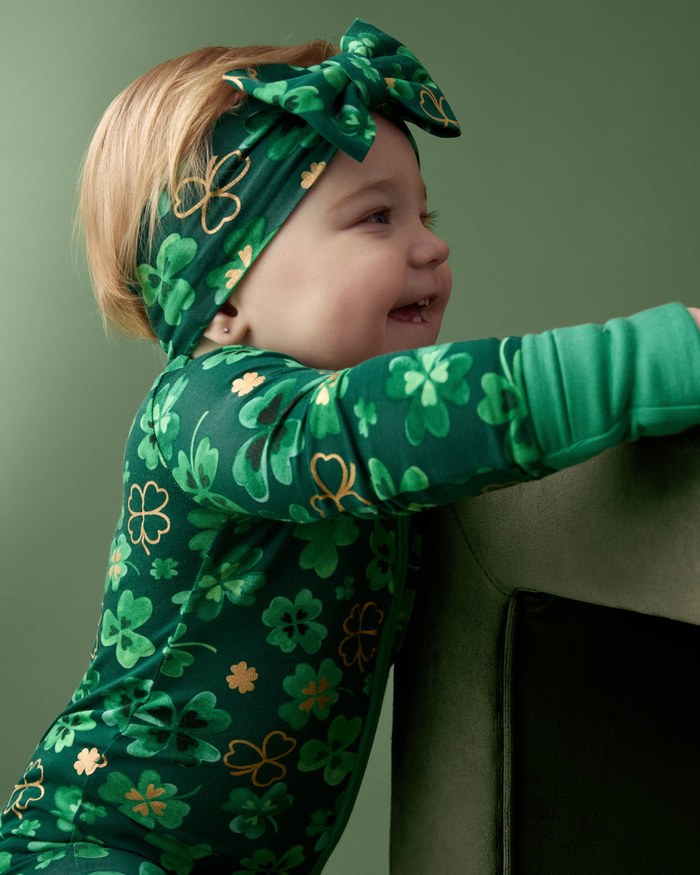 Baby wearing the Clover Cuties Luxe Bow Headband on a green back drop