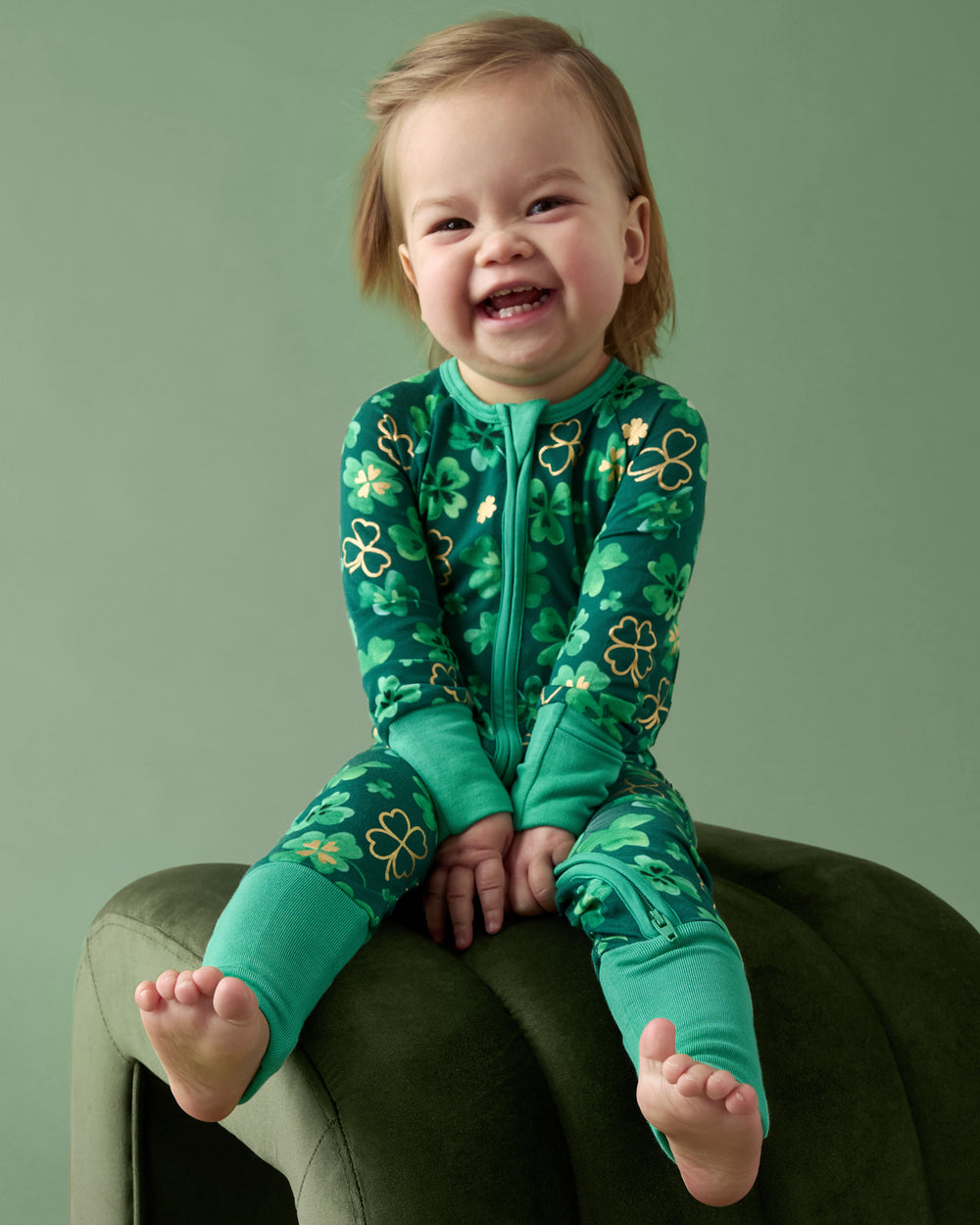 Child zipper on a green ottoman wearing the Clover Cuties Zippy