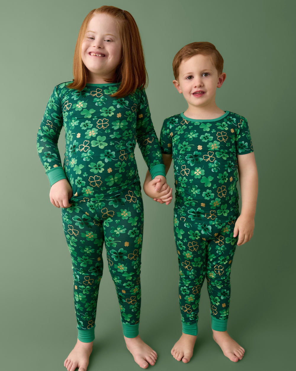 Two children wearing Clover Cuties Two-Piece Pajama Sets on a green background