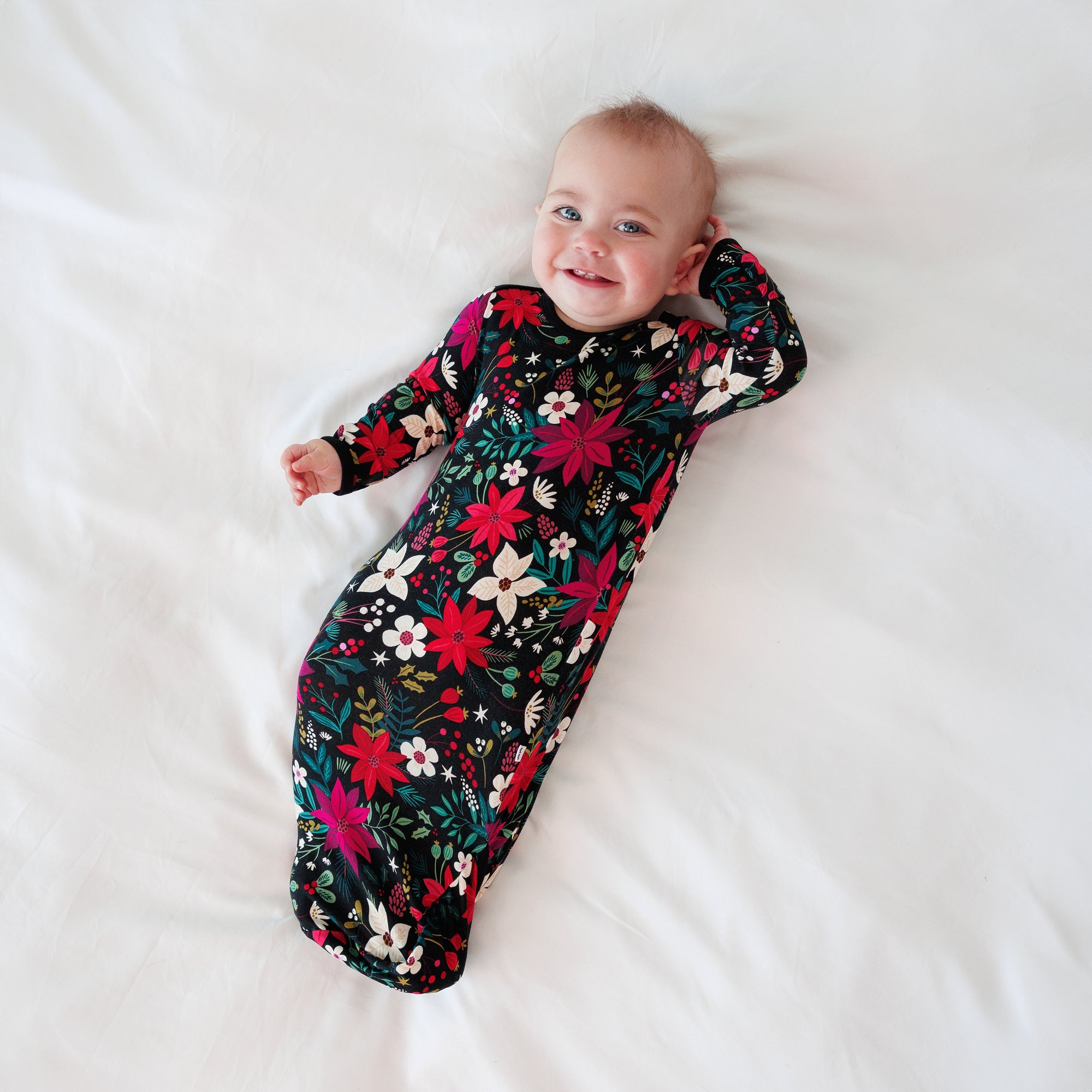 Top view image of a baby laying down and posing while in the Berry Merry Infant Gown