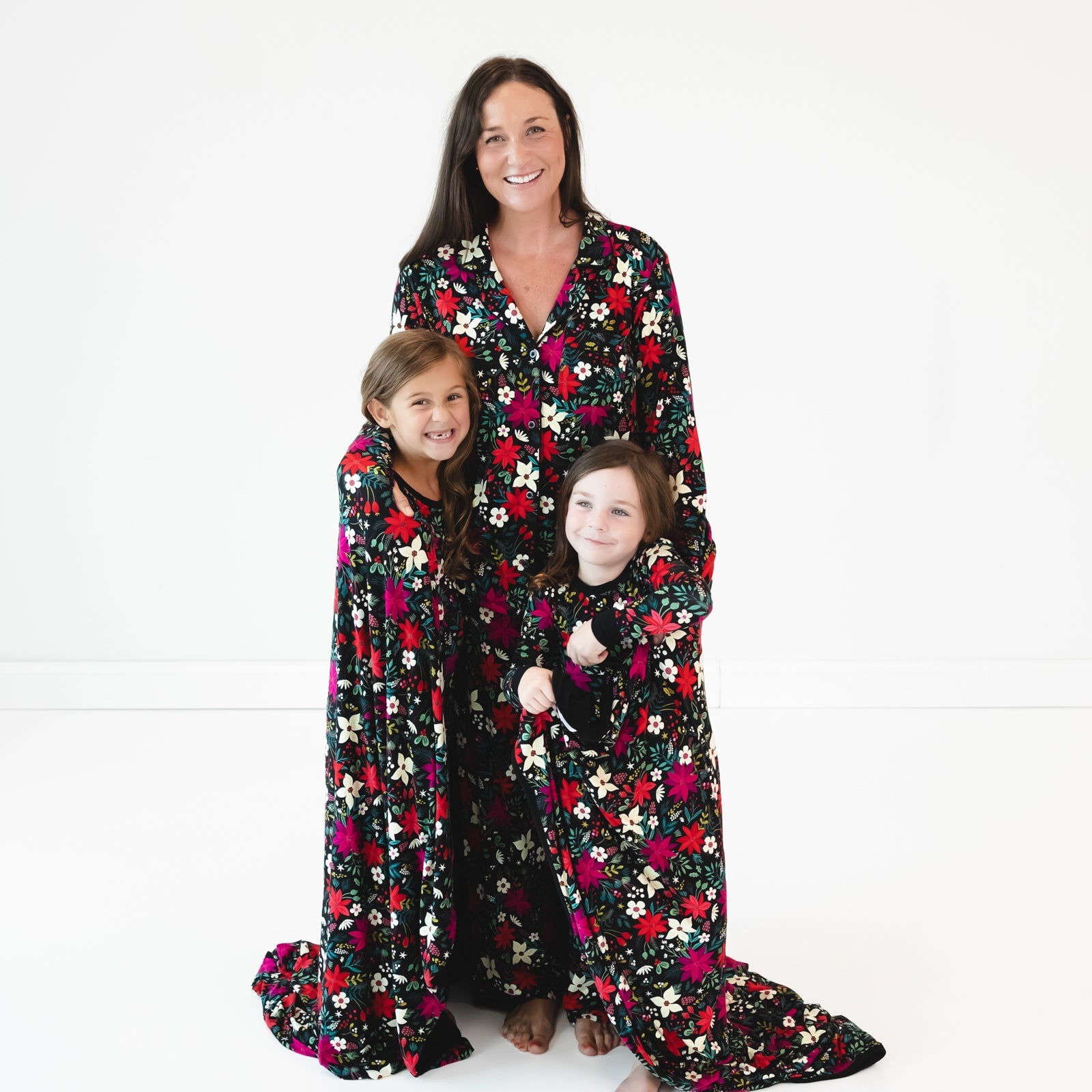 Mother with two daughters wrapped in the Berry Merry Oversized Cloud Blanket® and wearing matching Berry Merry pajamas