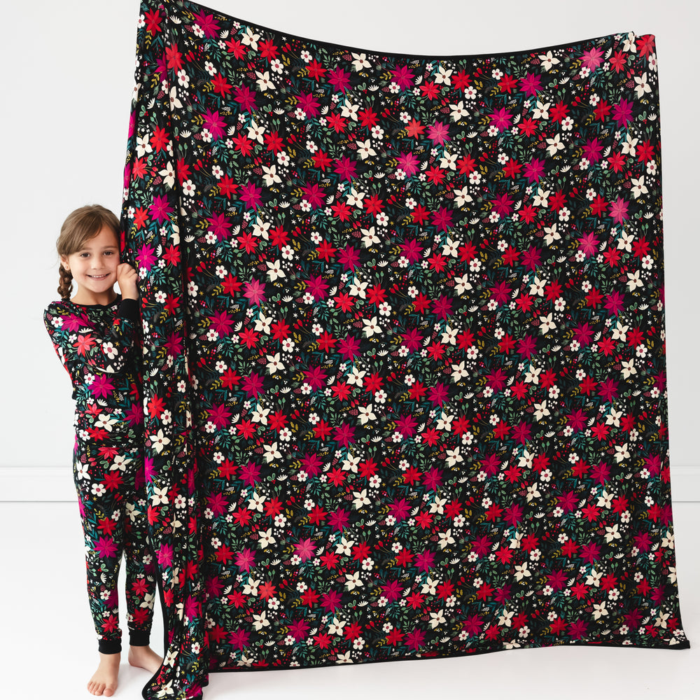 Image of a girl standing next to a stretched out Berry Merry Oversized Cloud Blanket® while wearing the Berry Merry Two-Piece Pajama Set