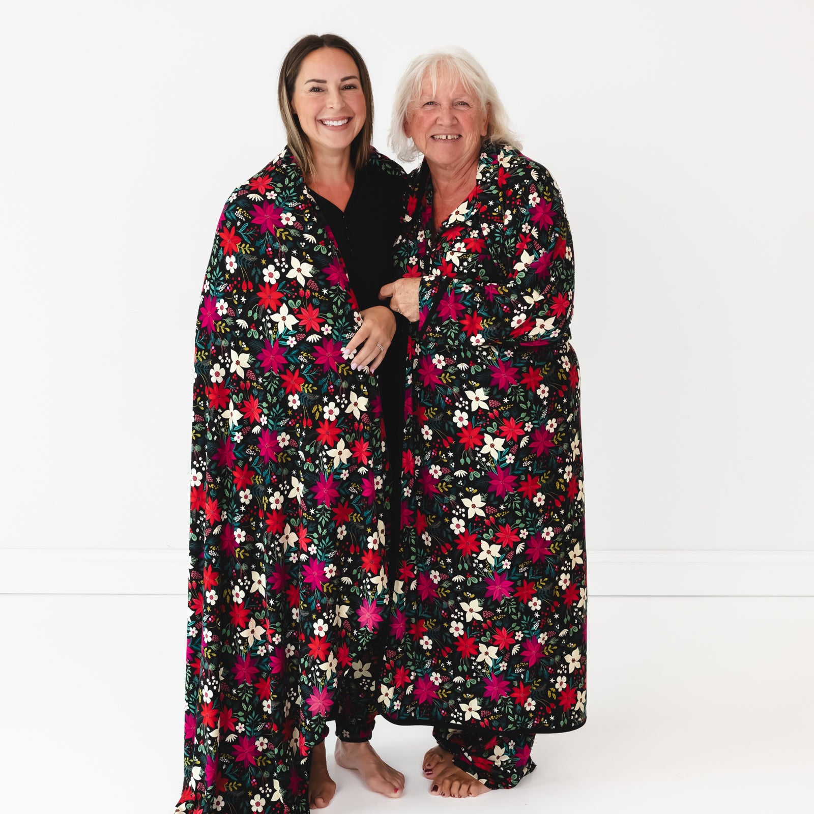 Female model on the left is wrapped in the Berry Merry Oversized Cloud Blanket® and elder female model on right is in the Berry Merry Women's Robe