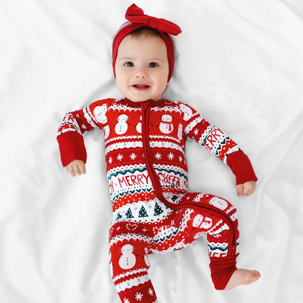 Child laying on a blanket wearing a Festive Fair Isle Zippy and Holiday Red Luxe Bow Headband