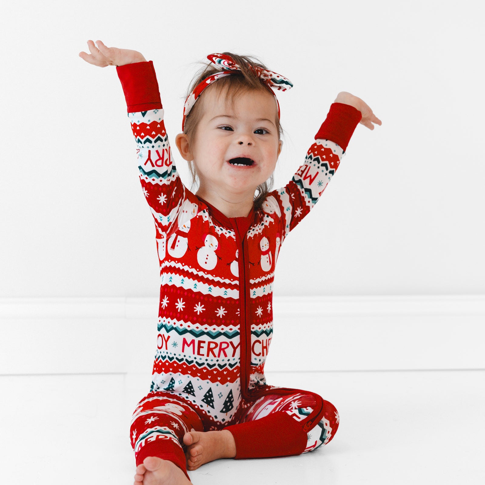 Child sitting on the ground wearing a Festive Fair Isle Luxe Bow Headband and Zippy