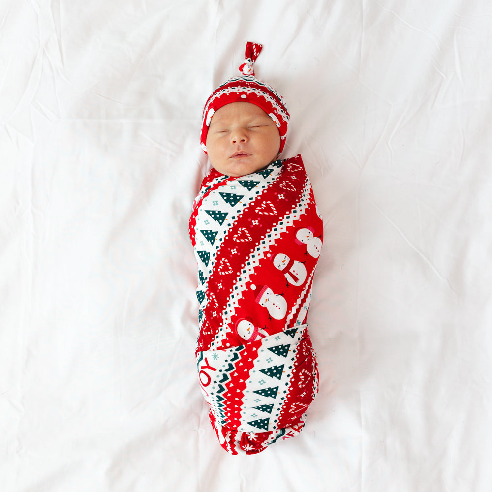 Image of an infant laying on a blanket swaddled in a Festive Fair Isle Swaddle & Hat Set