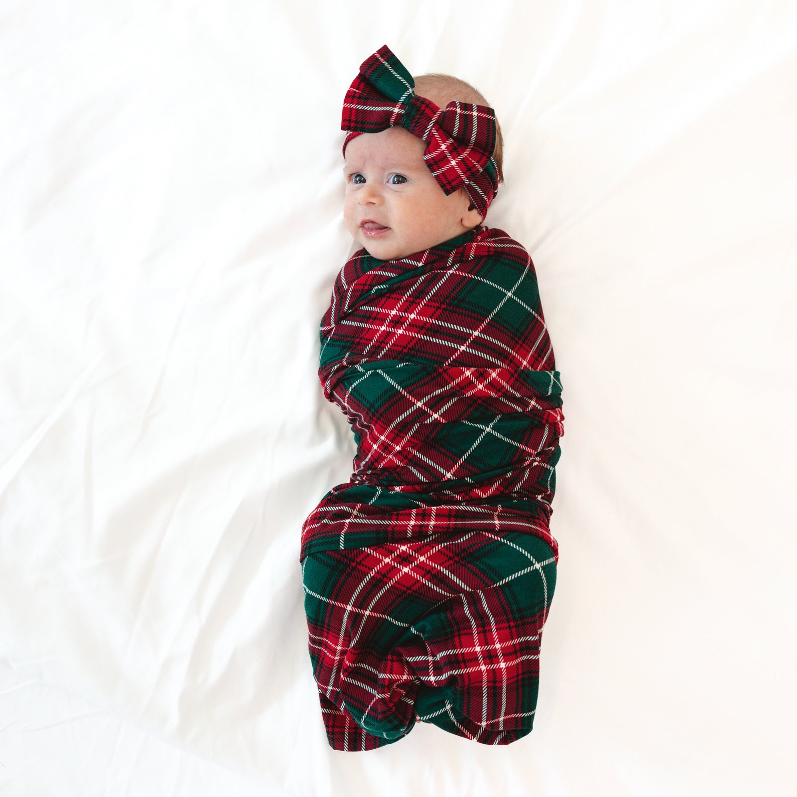 Infant laying on a blanket swaddled in a Fireside Plaid Swaddle & Luxe Bow Headband Set