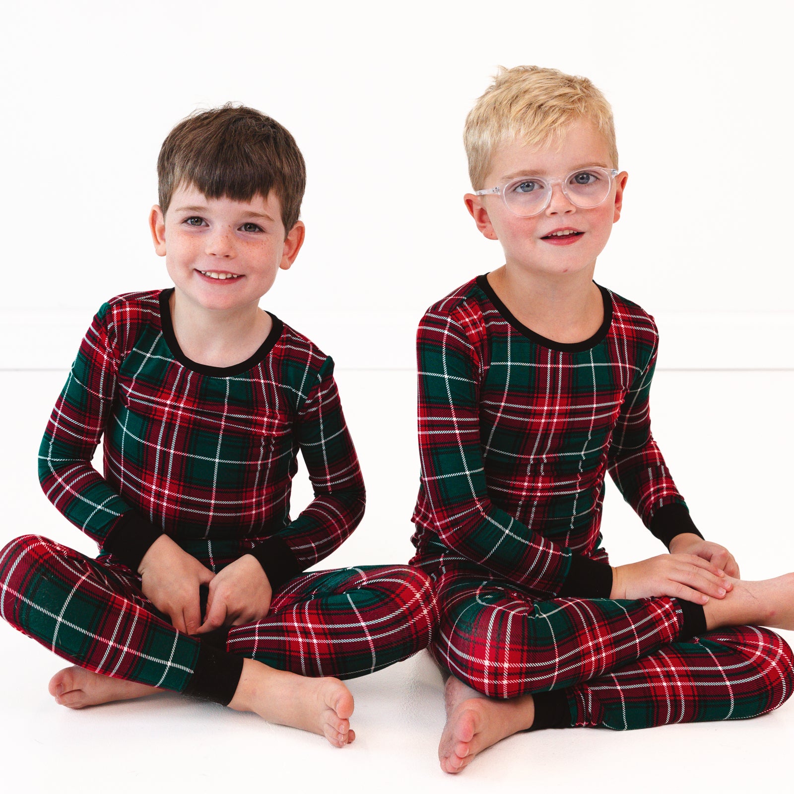 Two children sitting on the ground wearing Fireside Plaid Two-Piece Pajama Sets