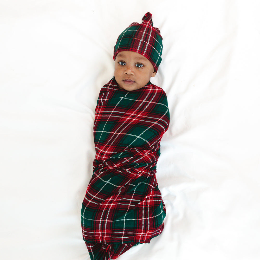 Infant laying on a blanket swaddled in a Fireside Plaid Swaddle & Hat Set