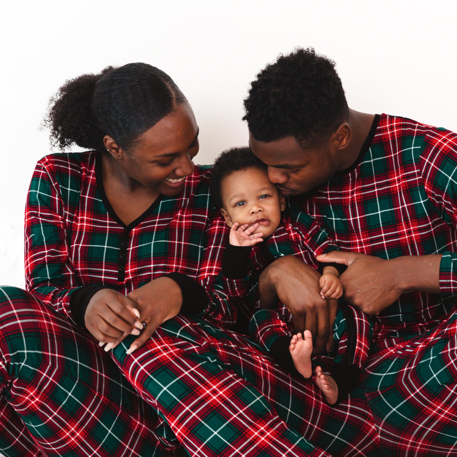 Family of three sitting on the ground wearing matching Fireside Plaid pajamas