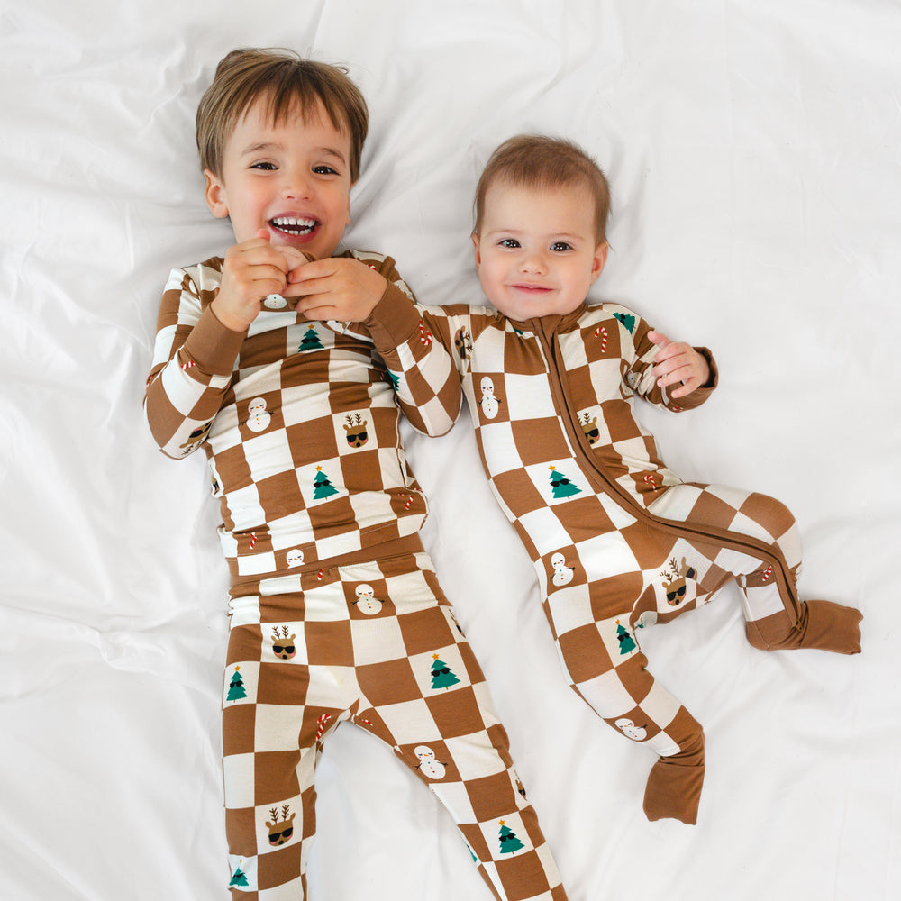 Top view image of boy on the left wearing the Holiday Checks Two-piece Pajama set and baby on the right is in the Holiday Checks Zippy 