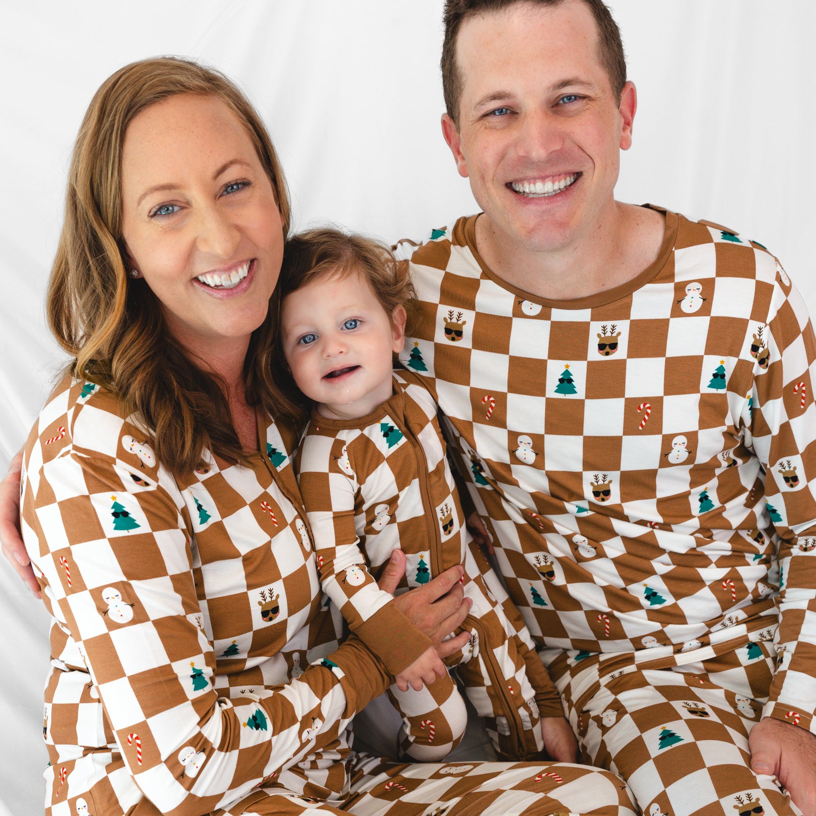 Female model on the left is wearing the Holiday Checks Women's Pajama Top. Baby in the middle is in the Holiday Checks Zippy and male model on the right is in the Holiday Checks Men's Pajama Top