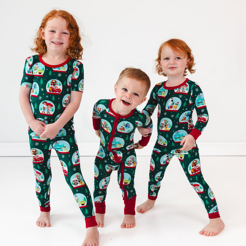 Smiling child on the left is wearing the Disney A Very Pixar Christmas Two-Piece Short Sleeve Pajama Set, boy in the middle is wearing the Disney A Very Pixar Christmas Zippy, while posing child on the right is wearing the Disney A Very Pixar Christmas Two-Piece Pajama Set