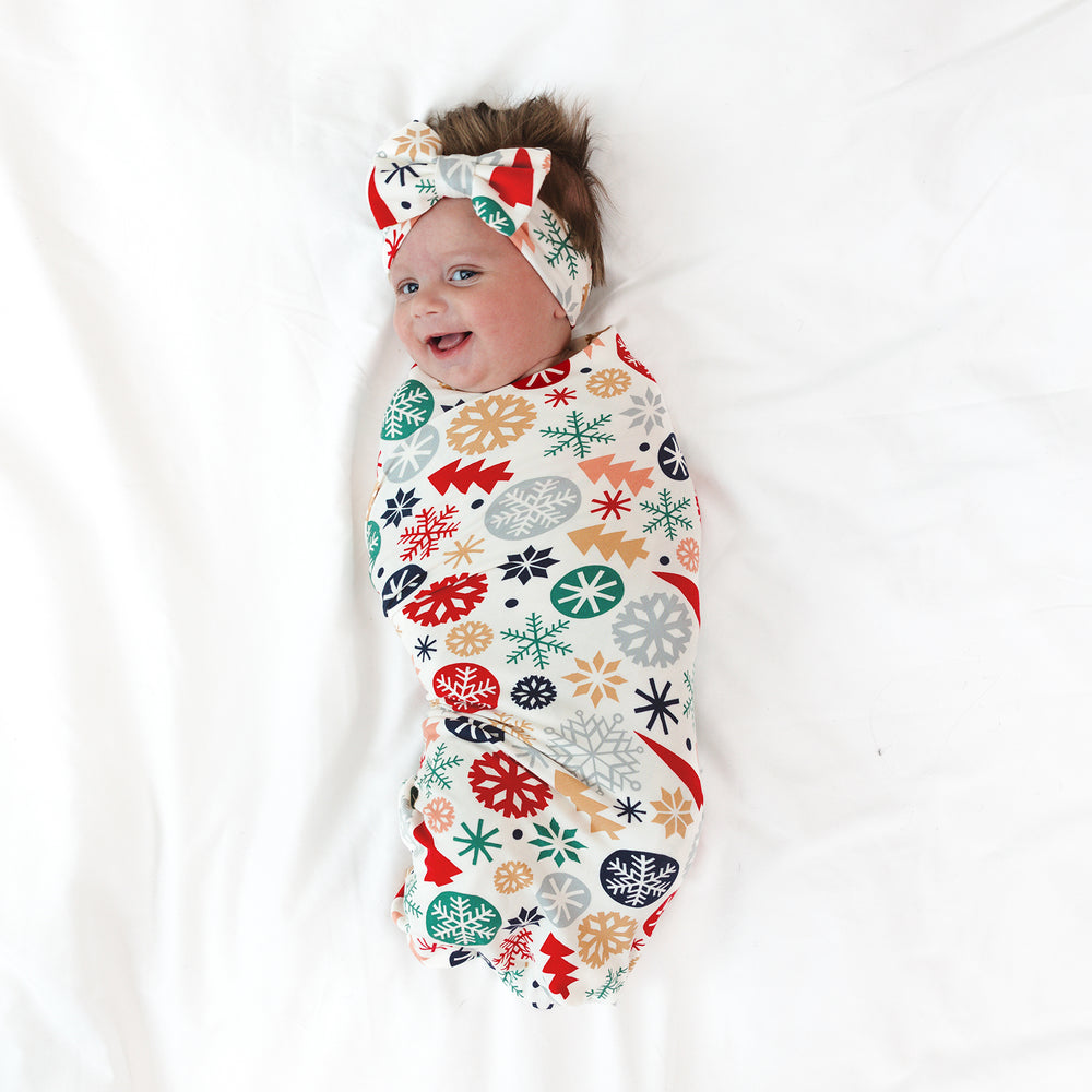 Alternative top view image of smiling baby wrapped in the Modern & Merry Swaddle & Luxe Bow Headband Set