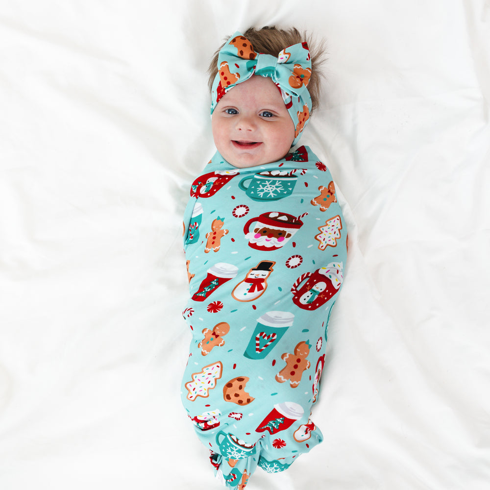 Image of an infant laying on a blanket swaddled in a Peppermint Mocha Swaddle & Luxe Bow Headband Set