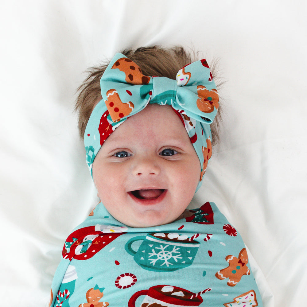 Close up image of an infant laying on a blanket swaddled in a Peppermint Mocha Swaddle & Luxe Bow Headband Set