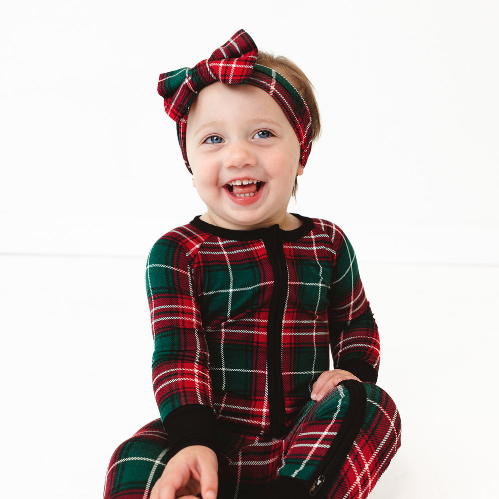 Child sitting on the ground wearing a Fireside Plaid Luxe Bow Headband and Zippy