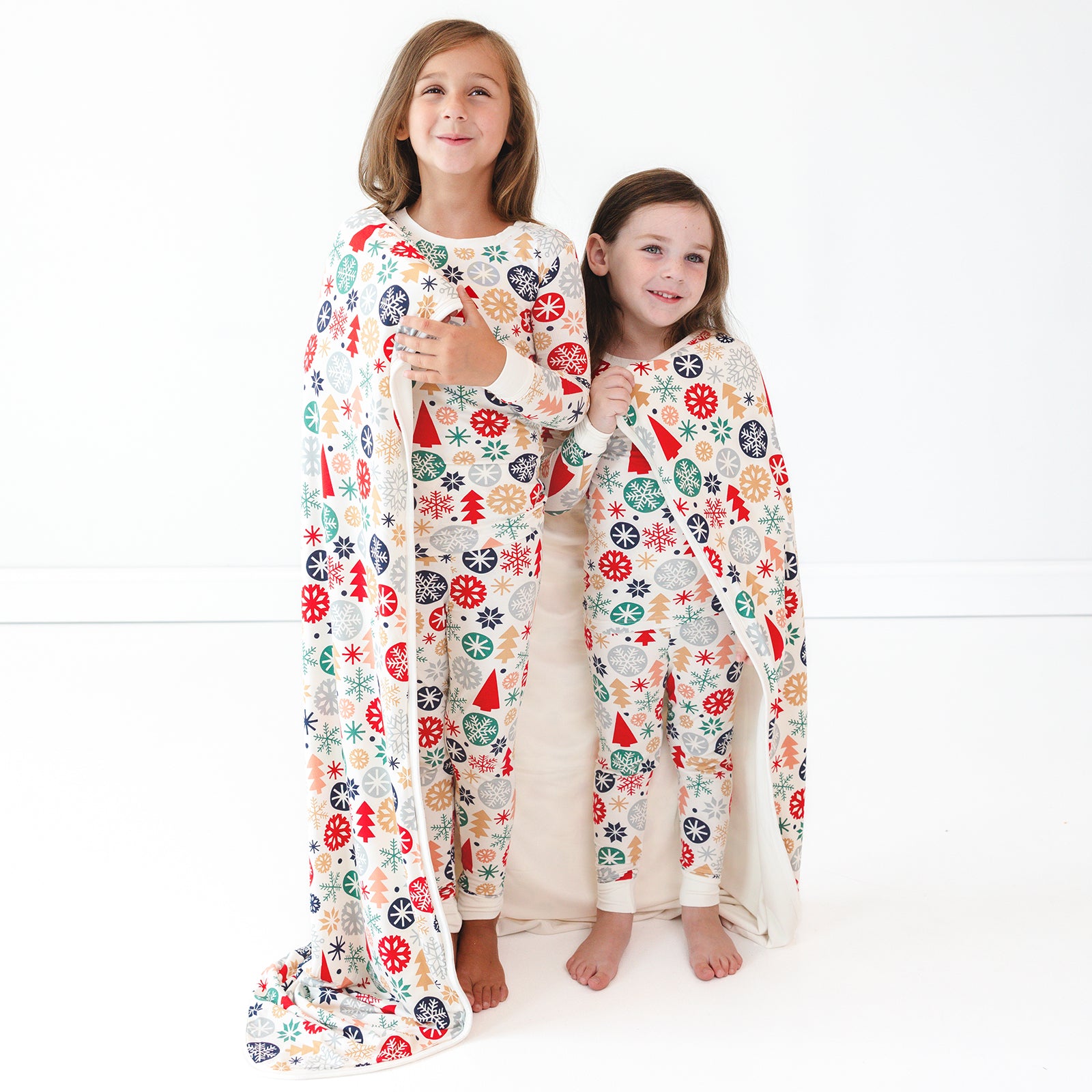 Two children wearing the Modern & Merry Two-piece Pajama Set and both wrapped in the Modern & Merry Large Cloud Blanket®