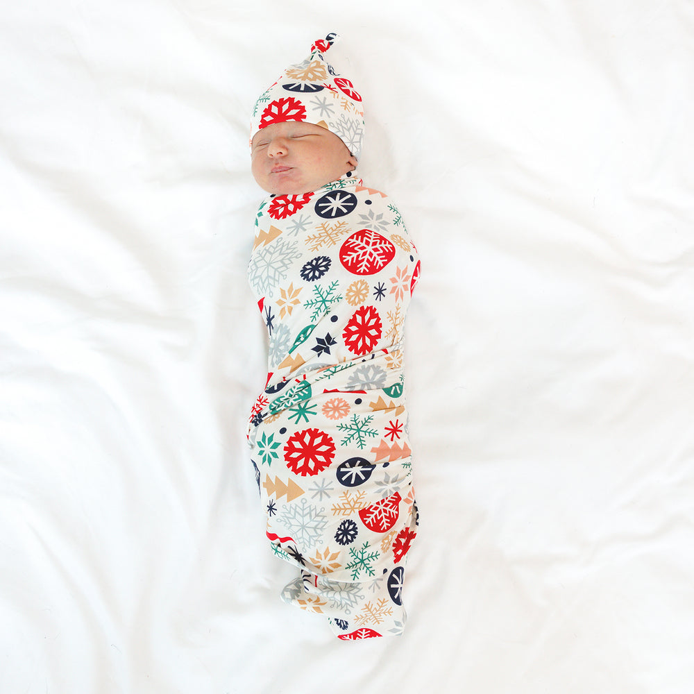 Top view image of baby laying down while wrapped in the Modern & Merry Swaddle & Hat Set