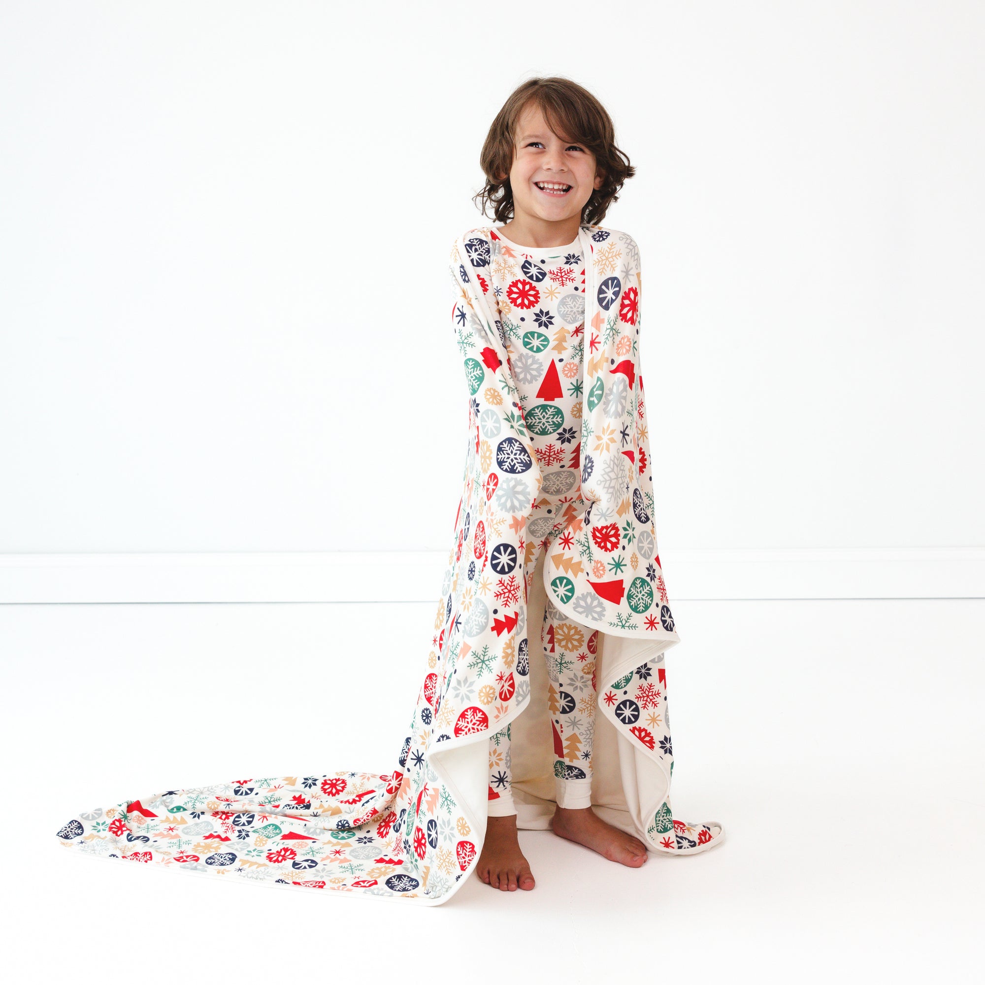 Smiing child wearing the Modern & Merry Two-piece Pajama Set while wrapped in the Modern & Merry Large Cloud Blanket®