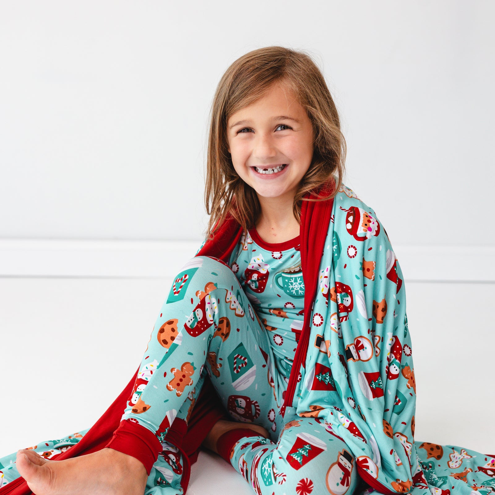 Child sitting on the ground wrapped up in a Peppermint Mocha Large Cloud Blanket and wearing matching pajamas.