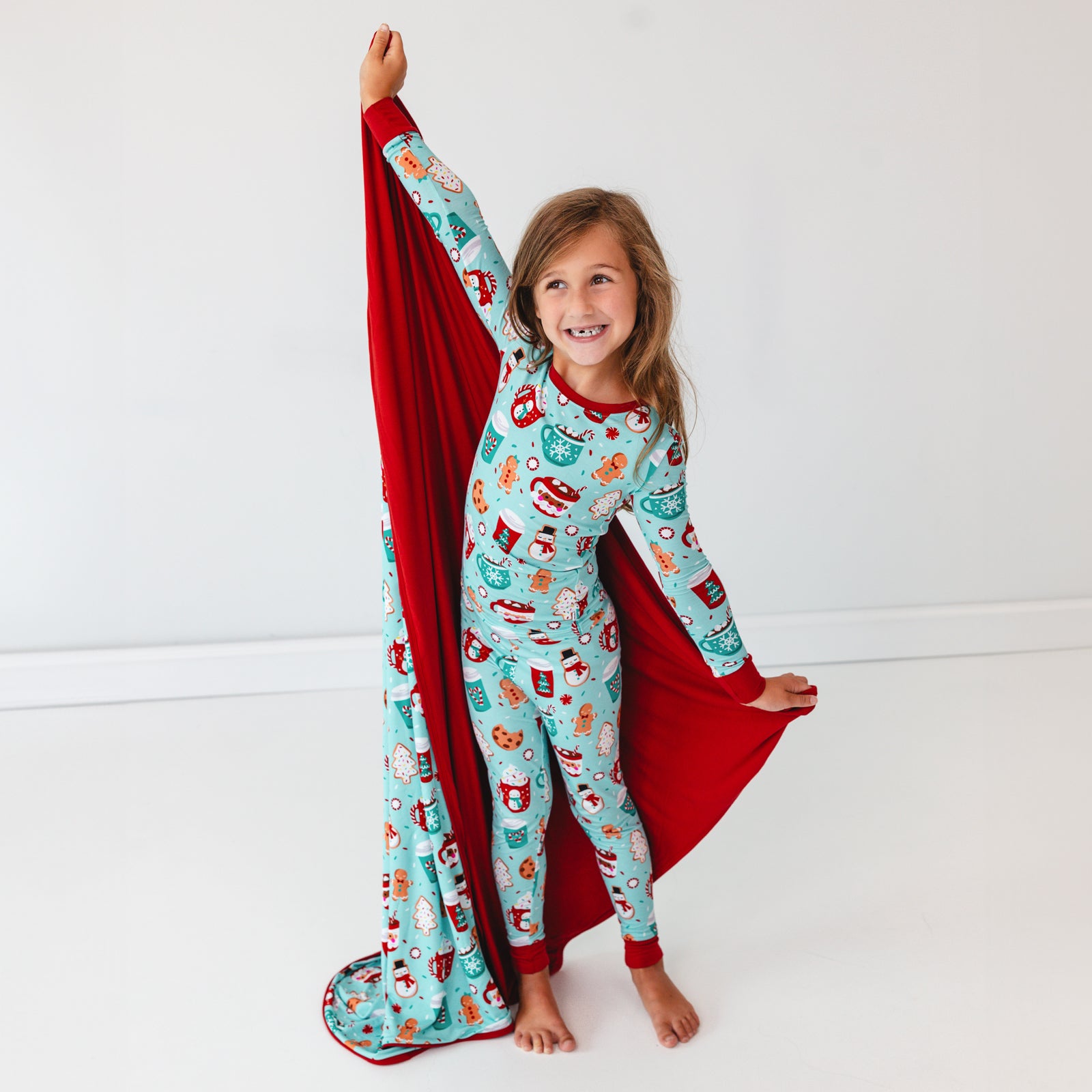 Image of a child wearing a Peppermint Mocha Two-Piece Pajama Set holding a matching Large Cloud Blanket out behind them.